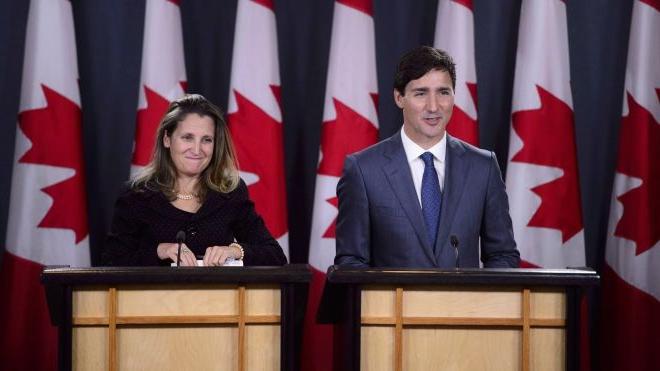 “贾斯汀·特鲁多和克里斯蒂亚·弗里兰站在加拿大国旗前的领奖台上”